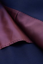 Close-up, top-down view of the inside lining and outer fabric of the Sipario Smart-casual jacket 'Ivan' dark blue, showcasing its deep blue pure wool exterior and maroon striped, slightly elasticated soft fabric lining with detailed stitching. A stylish o