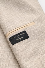 Nahaufnahme des beige melierten Tagliatore Sakkos 'Monte Carlo' mit Unconstructed-Verarbeitung, weichem Griff, Strukturgewebe und Markenlabel, fotografiert aus schräger Perspektive.