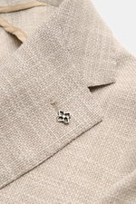 Nahaufnahme des fallenden Revers mit markentypischem Pin des Tagliatore Sakkos 'Monte Carlo' beige meliert aus Wolle, Baumwolle und Seide.