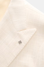 Tagliatore Sakko 'Vesuvio' creme Detailaufnahme des zweireihigen Drei-Knopf-Sakkos mit Spitzrevers und markantem Pin, textile Webstruktur sichtbar.
