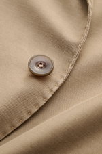 Nahaufnahme des taupefarbenen Santaniello Sakkos mit Fokus auf den Knopf und die feine Baumwoll-Leinen-Mohair-Struktur, Slim Fit, zwei Knöpfe, fallendes Revers, klassische Brust- und Hüfttaschen, Kissing Buttons, Seitenschlitze, Unconstructed Design, drei