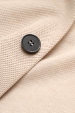 Close-up front view of the Harris Wharf London Knit blazer beige showing its textured pure piqué cotton fabric and a black four-hole button. 

<p>HARRIS WHARF LONDON has chosen a high-quality cloth from Loro Piana for this relaxed knit blazer. Pure cotton