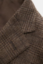 Nahaufnahme des fallenden Revers und der Brusttasche eines graubraun karierten Corneliani Sakkos aus Wolle-Cashmere-Mix mit tonalem Prince-of-Wales Muster, fotografiert schräg von oben.