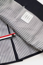 Innenansicht des Thom Browne Sakko navy, fotografiert aus Nahaufnahme schräg von oben, mit gestreiftem Futter, Ripsband in Tricolore und Innentaschen.