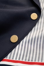 Nahaufnahme des Thom Browne Sakko navy aus reiner Wolle mit goldfarbenen Kissing Buttons, maritim monochrom, feinem Twill, weichem Griff, Ripsband in Tricolore, kontrastfarbenem Futter und Streifenmuster, fotografiert von oben.