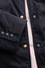 Nahaufnahme der Thom Browne Daunenjacke navy von oben, zeigt glatte Microfaser, Knöpfe, Tricolore-Ripsband und Daunenfüllung.