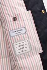 Nahaufnahme der Thom Browne Daunenjacke navy von innen mit gestreiftem Futter, Label und Knopf, zeigt hochwertige Microfaser und Daunenfüllung.