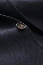 Close-up of a button on the Stile Latino Sakko 'Vincenzo' navy/schwarz gemustert fabric showing classic herringbone pattern and soft wool-cashmere blend texture, photographed from a macro side angle. Spürbaren Luxus präsentiert STILE LATINO mit seinem edl