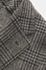 Close-up angled view of the Tagliatore Blazer grey/black checked showing soft virgin wool and cashmere mix, Prince of Wales pattern, slim fit, tailored two-button style, notched lapel with brand-typical pin, classic breast pocket, patch hip pockets, rear 