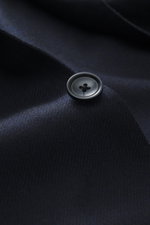 Close-up view of a black button on the Tagliatore Navy Blazer made of wool with cashmere content, soft touch, slim fit, tailored two-button style, notched lapel with brand-typical pin, classic breast pocket, patch hip pockets, unfinished sleeve cuffs, bac