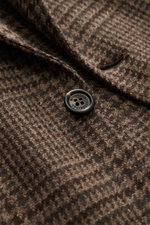 Close-up angled view of the Brunello Cucinelli Blazer navy/black checkered fabric and button, featuring virgin wool with cashmere content, soft touch, slim fit, tailored three-button style, notched lapel, classic breast pocket, hip pockets with flap, tick