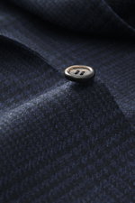 Close-up from an angled side view of a pure wool Canali Blazer navy/black checked with Prince-of-Wales pattern, soft touch, slim fit, tailored two-button style, notched lapel, classic breast pocket, hip pockets with flap, unfinished sleeve cuffs, rear sid