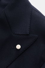 Nahaufnahme des Luigi Bianchi Sakko navy aus reiner Schurwolle mit Slim Fit, zweireihigem Drei-Knopf-Stil, Spitzrevers und weißem Revers-Pin, fotografiert von oben.
