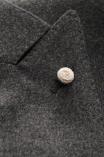Nahaufnahme des spitz zulaufenden Revers mit weißem Pin und feiner Struktur des Luigi Bianchi Sakko dunkelgrau meliert aus Schurwolle und Cashmere, Slim Fit, zweireihiger Drei-Knopf-Stil, Knöpfe mit Wappen-Emblem, halb gefüttert.