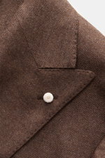 Nahaufnahme des zweireihigen Luigi Bianchi Sakko braun meliert mit Spitzrevers und weißem Knopf, schräg von oben fotografiert.