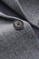 Nahaufnahme eines schwarzen Knopfs auf dem graublau gemusterten Circolo 1901 Jersey-Sakko, Jersey aus Baumwolle mit Stretch, Print in Weboptik, Slim Fit, taillierter Zwei-Knopf-Stil, fallendes Revers, fotografiert aus schräger Perspektive.