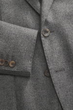 Close-up front view of the Santaniello Blazer grey melange, showing pure wool fabric, soft touch, slim fit, notched lapel, two-button style, classic breast pocket, patch hip pockets, kissing buttons, rear side vents, unconstructed design, and two inner po
