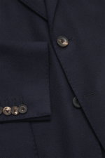 Close-up front angle of the Santaniello Blazer navy showing pure wool fabric, soft touch, slim fit, tailored two-button style, notched lapel with label pin, classic breast pocket, patch hip pockets, kissing buttons, rear side vents, unconstructed design, 