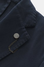 Nahaufnahme des fallenden Revers mit Label-Pin des Santaniello Sakko navy aus leicht elastischem Baumwoll-Twill, fotografiert schräg von oben.
