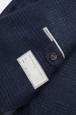 Brunello Cucinelli Navy/grey-blue checked blazer close-up from above, showing wool with cashmere, soft touch, Prince-of-Wales pattern, slim fit, three-button style, notch lapel, classic breast pocket, hip pockets with flap, small ticket pocket, sleeve cuf