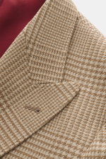 Close-up front angle of Brunello Cucinelli Beige/light brown checked blazer showcasing Prince of Wales pattern, soft wool-cashmere mix, slim fit, three-button style, notched lapel, classic breast pocket, hip pockets with flaps, small ticket pocket, sleeve