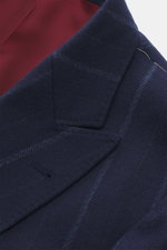 Close-up photo from above of the Brunello Cucinelli Navy striped blazer showing peak lapels, soft virgin wool and cashmere fabric with subtle stripes, classic breast pocket, and burgundy half lining. Slim Fit, double-breasted three-button style, hip pocke