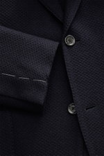 Close-up front view of the Lardini Knitted Blazer Navy, knit from wool with a soft touch, slim fit, draped lapel with flower pin, tailored two-button style, classic breast pocket, patch hip pockets, unfinished sleeve cuffs, rear side vents, unconstructed 