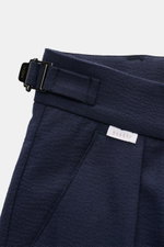 Nahaufnahme der Taille der 04651/ A trip in a bag Seersucker-Hose navy aus Wolle und Microfaser mit Side-Adjuster, Bundknopf, Reißverschluss, doppelter Bundfalte, französischen Taschen, Leistentaschen, fixiertem Saumaufschlag und dezenter Weblabel.