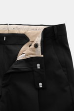 PT Torino Wool Pants 'Rebel Fit' Black shown from a close-up front angle with zipper open, showcasing elastic virgin wool, tapered fit, waistband hook, French pockets, back pockets with button flap, single waistband pleat, small metal initial, and fixed h