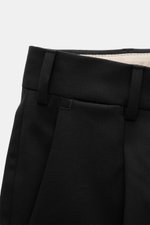 PT Torino Wool Pants 'Rebel Fit' Black shown from close-up front waist perspective, featuring elastic virgin wool, tapered fit, single pleat, French pockets, back flap pockets, zipper, hook, metal initial, and fixed hem cuff.