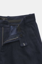 Close-up front view of Percival Trousers 'Stanley Herringbone' dark blue, showcasing zipper, waistband hook, single pleat, French pockets, piped back pockets, tapered fit, regular thigh width, ankle-length, made of soft-touch mix of microfiber, wool, and 