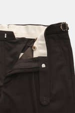 Nahaufnahme der geöffneten Taille der GTA Wollhose 'Herrick' dunkelbraun von vorne, zeigt Reißverschluss, Bundknopf, elastischen Einsatz im Bund, Side Adjuster, doppelte Bundfalte, französische Taschen und kleines Logo-Detail, gefertigt aus leicht elastis