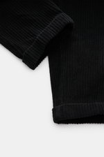 Close-up view of the lower legs of 04651/ A trip in a bag Corduroy cargo pants black, showing wide wale cotton corduroy fabric with slight stretch, soft feel, tapered fit, regular thigh width, ankle length, slightly tapered cut, fixed hem turn-up, and vis