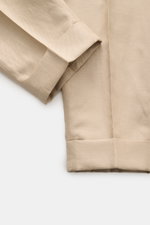 Nahaufnahme der beige PT Torino Hose 'Carrot Fit' mit kurzem, schmal zulaufendem Bein, fixiertem Saumaufschlag und markanter Köperstruktur aus Schurwolle und Leinen, fotografiert von oben.