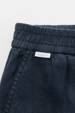 Close-up front view of 04651/ A trip in a bag Leinen-Jogpants 'Linen Pants' navy showing elastic waistband, pure linen fabric, typical texture, tapered fit, regular thigh width, ankle length, straight cut, small woven label, French pockets, and patch back