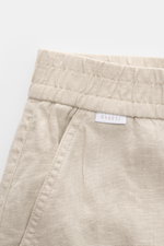 Close-up front view of 04651/ A trip in a bag Leinen-Jogpants 'Linen Pants' beige showing elastic waistband, French pocket, and linen texture. Perfect for warm days: pure linen, typical material structure, tapered fit, regular thigh width, ankle length, s