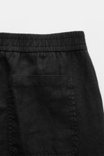Close-up rear view of 04651/ A trip in a bag Leinen-Jogpants 'Linen Pants' schwarz showing elastic waistband, pure linen fabric, typical texture, patch back pocket, and black color. Perfect for warm days: linen jogpants ideal for summer, tapered fit, regu