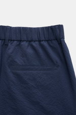 Close-up rear view of 04651/ A trip in a bag Seersucker trousers 'Technical Seersucker' navy, showing fine typical microfibre seersucker texture, robust fabric, elastic waistband with belt loops, single hip pocket, subtle woven label at the waist. Feature