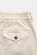 Detailaufnahme der Rückseite der beige 04651/ A trip in a bag Baumwoll-Jogpants "Flex Light" mit elastischem Bund, geknöpfter Gesäßtasche und weichem Griff.