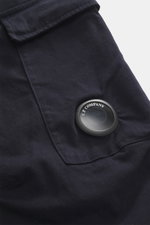 Nahaufnahme der C.P. Company Cargohose navy mit labeltypischem Linsendetail, Cargo-Tasche, Reißverschluss, Bundknopf, reine Baumwolle, leichter Stretch, weicher Griff, Regular Fit, schmal zulaufend, Taschen in der Seitennaht, paspelierte Gesäßtaschen, aus