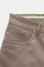 Close-up front-side view of Jacob Cohen Chino 'Bard' taupe, showing slim-fit twill cotton fabric, button fly, five-pocket style, coin pocket with initial, back pockets with stitching, and suede leather patch.

<p>Modern luxury for everyday wear: The premi