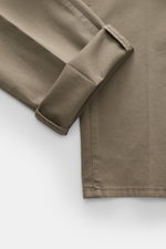 Brunello Cucinelli Chinos 'Italian Fit' sage shown from a close-up top-down angle, highlighting elasticated cotton twill fabric, soft feel, garment-dyed finish, tapered cut, and detailed stitching on folded hem. These chinos from luxury label BRUNELLO CUC
