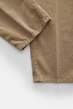 Close-up of Brunello Cucinelli light brown corduroy pants showing fabric texture and stitching from top-down perspective, highlighting soft pure cotton, garment dyed material with single pleat and tapered regular fit.