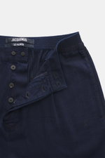 Jacquemus Denim-Jogpants dunkelblau, Nahaufnahme von Bund und Button Fly, Denim aus reiner Baumwolle, weicher Griff, Loose Fit, gerader Schnitt, elastischer Bund, Gesäßtaschen, Weblabel.