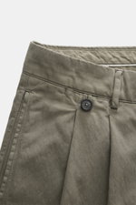 Close-up front view of Massimo Osti Studio Trousers grey green, featuring mix of cotton and microfiber, smooth touch, loose fit, straight cut, button fly, small watch pocket, double waistband pleat, piped pockets, back pockets with flap and button, and so