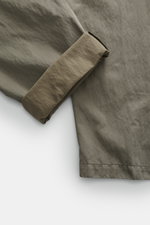 Massimo Osti Studio Trousers grey green shown from a close-up top-down view, featuring a mix of cotton and microfiber, smooth touch, loose fit, straight cut, button fly, small watch pocket, double waistband pleat, piped pockets, back pockets with flap and