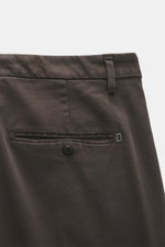 Nahaufnahme der Dondup Baumwollhose 'Spiritissimo' dunkelbraun, schmal zulaufend mit weicher Haptik, markanter Webstruktur, paspelierter Gesäßtasche mit Knopf und Metallinitial, fotografiert aus seitlicher Rückansicht.
