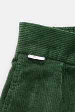 Green corduroy fabric close-up with visible ribs and a white label, photographed from a top-down perspective.  
<p>These corduroy pants by 04651/ A TRIP IN A BAG are made of cotton corduroy with a seersucker backside, providing special wearing comfort an
