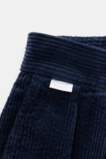 Close-up front top view of 04651/ A trip in a bag Corduroy pants navy showing soft wide cotton corduroy fabric with ribbed texture and label.  

These corduroy pants by 04651/ A TRIP IN A BAG are made of wide cotton corduroy with a seersucker backing, pro