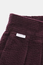 Nahaufnahme aus seitlicher Perspektive der breiten Bundfalte und des Labels der bordeauxfarbenen 04651/ A trip in a bag Cordhose aus softem Baumwoll-Cord.